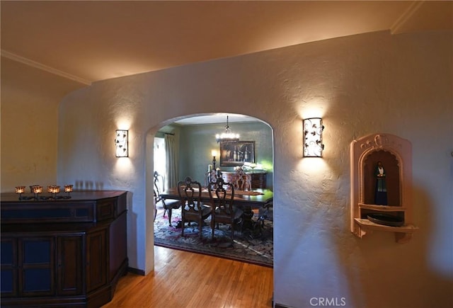 dining room featuring crown molding, a textured wall, light wood-style floors, arched walkways, and a chandelier
