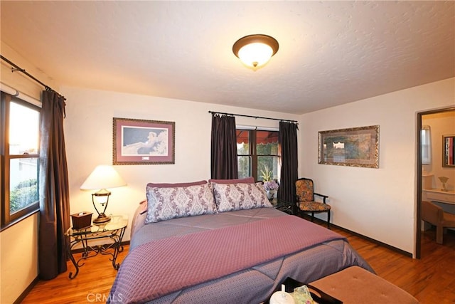 bedroom with baseboards, multiple windows, and wood finished floors