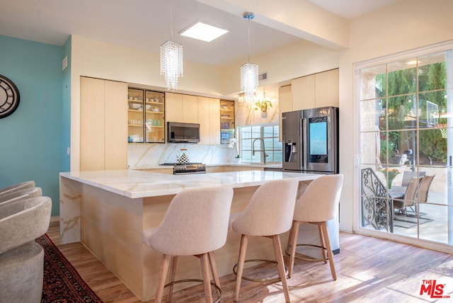 kitchen featuring a kitchen breakfast bar, kitchen peninsula, light stone countertops, pendant lighting, and appliances with stainless steel finishes