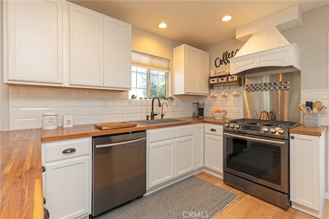 kitchen featuring premium range hood, sink, butcher block countertops, stainless steel appliances, and white cabinets