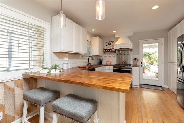 kitchen with butcher block counters, premium range hood, hanging light fixtures, and white cabinets