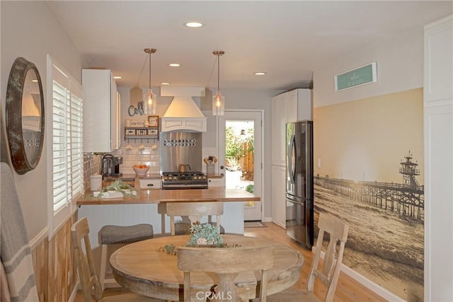 kitchen with decorative backsplash, decorative light fixtures, custom exhaust hood, stainless steel appliances, and white cabinetry