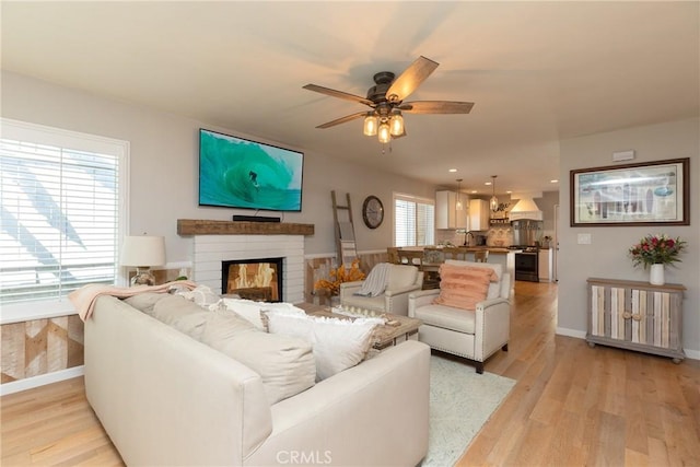 living room with ceiling fan, light hardwood / wood-style floors, and a brick fireplace