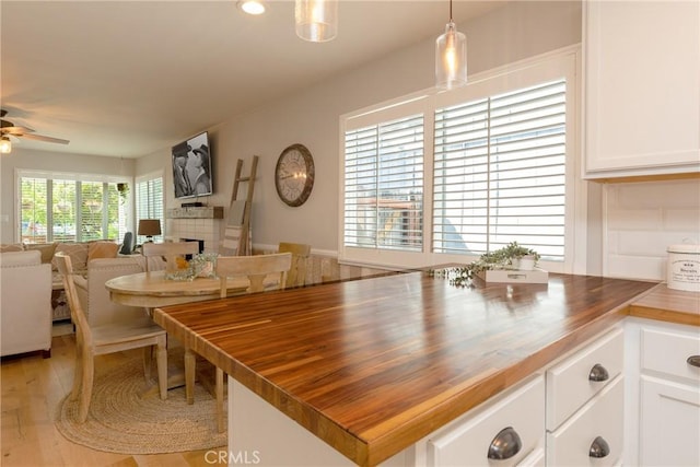 dining space featuring ceiling fan, a tiled fireplace, and light wood-type flooring