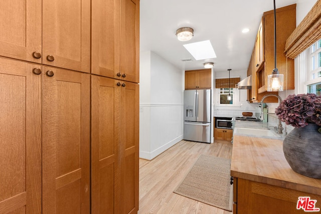 kitchen featuring extractor fan, pendant lighting, stainless steel fridge, a skylight, and sink