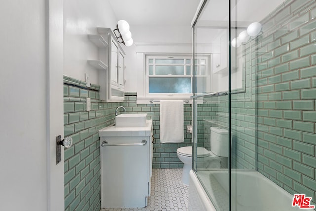 full bathroom featuring tile walls, combined bath / shower with glass door, toilet, tile patterned floors, and vanity