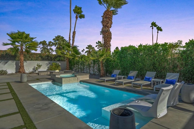 pool at dusk with a patio and an in ground hot tub