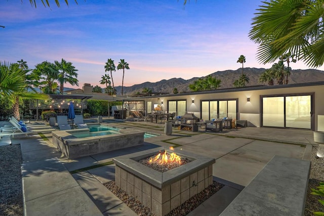 pool at dusk featuring an in ground hot tub, a patio, an outdoor fire pit, and a mountain view