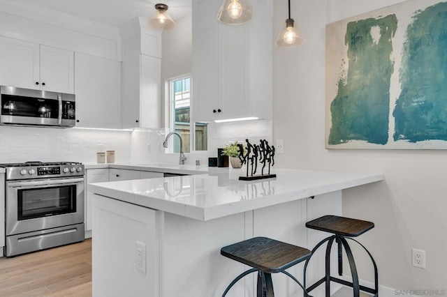 kitchen with white cabinetry, a breakfast bar, kitchen peninsula, pendant lighting, and appliances with stainless steel finishes