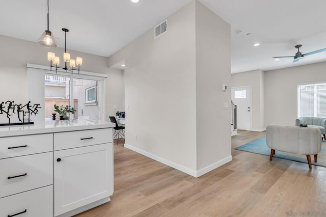 interior space with ceiling fan with notable chandelier, light wood-type flooring, hanging light fixtures, and white cabinetry