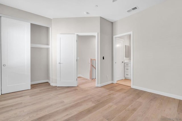 unfurnished bedroom with ensuite bathroom, light wood-type flooring, and a closet