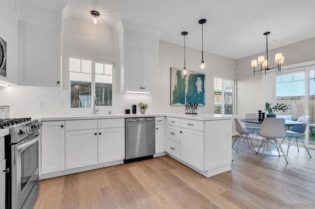 kitchen featuring sink, decorative light fixtures, white cabinetry, kitchen peninsula, and appliances with stainless steel finishes