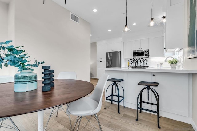 kitchen featuring kitchen peninsula, hanging light fixtures, stainless steel appliances, backsplash, and white cabinetry