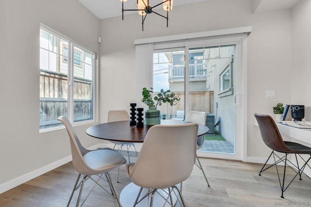 dining area with light wood-type flooring, a healthy amount of sunlight, and a notable chandelier