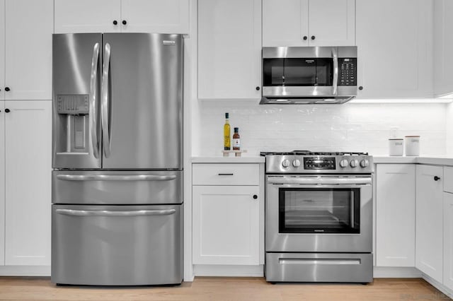 kitchen featuring decorative backsplash, white cabinetry, light wood-type flooring, and appliances with stainless steel finishes