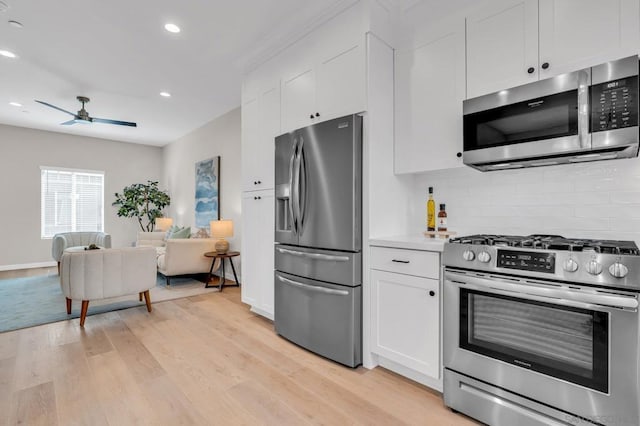 kitchen with appliances with stainless steel finishes, ceiling fan, white cabinets, light hardwood / wood-style flooring, and tasteful backsplash