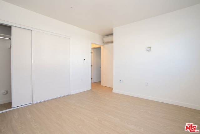 unfurnished bedroom with a wall mounted air conditioner, a closet, and light hardwood / wood-style flooring