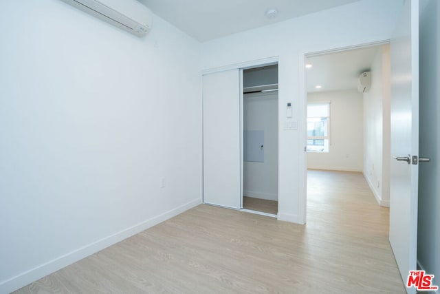 unfurnished bedroom with a closet, light wood-type flooring, and a wall mounted AC