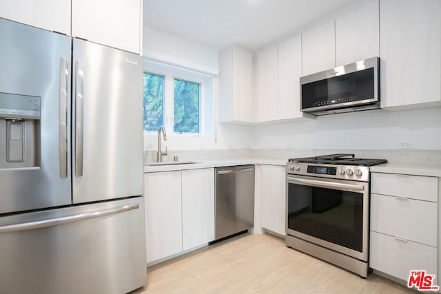 kitchen with stainless steel appliances, white cabinets, sink, and light hardwood / wood-style flooring