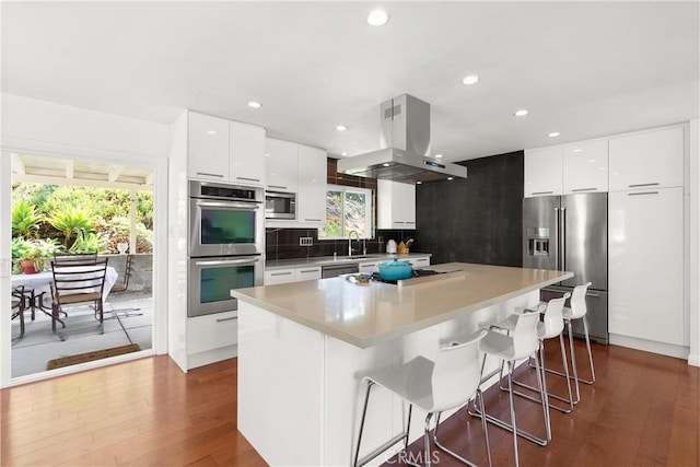 kitchen featuring appliances with stainless steel finishes, white cabinetry, island exhaust hood, and a kitchen bar