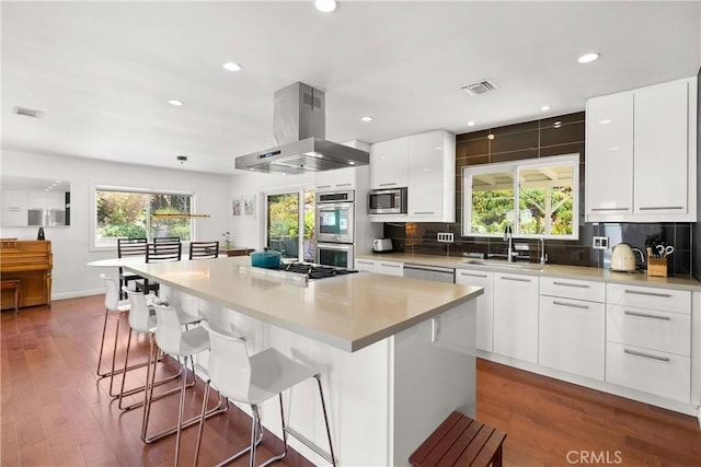 kitchen with island exhaust hood, stainless steel appliances, a center island, white cabinets, and sink