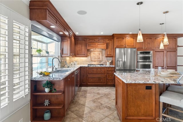 kitchen featuring light stone countertops, pendant lighting, a kitchen island, appliances with stainless steel finishes, and sink