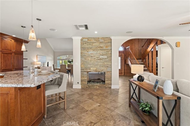 kitchen featuring light stone countertops, decorative light fixtures, lofted ceiling, a breakfast bar area, and a stone fireplace