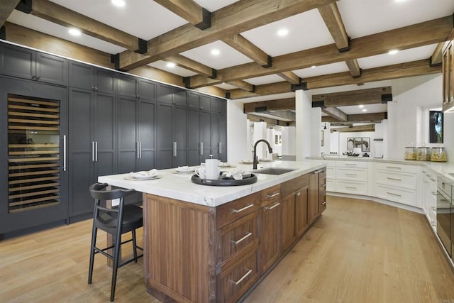 kitchen with beamed ceiling, white cabinetry, sink, beverage cooler, and a large island with sink