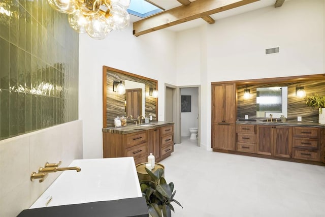 bathroom with a skylight, a chandelier, vanity, toilet, and beam ceiling