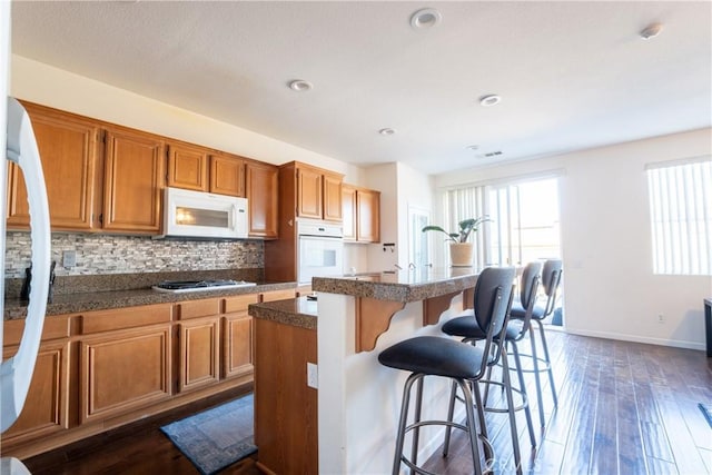 kitchen featuring dark wood-type flooring, white appliances, tasteful backsplash, and a kitchen island