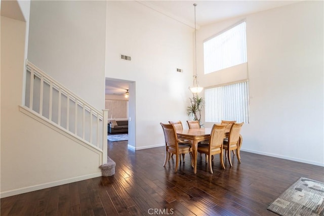 dining room with dark wood-type flooring, a towering ceiling, and ceiling fan