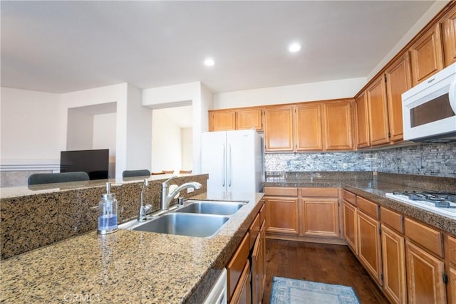 kitchen featuring light stone countertops, white appliances, decorative backsplash, sink, and dark hardwood / wood-style floors