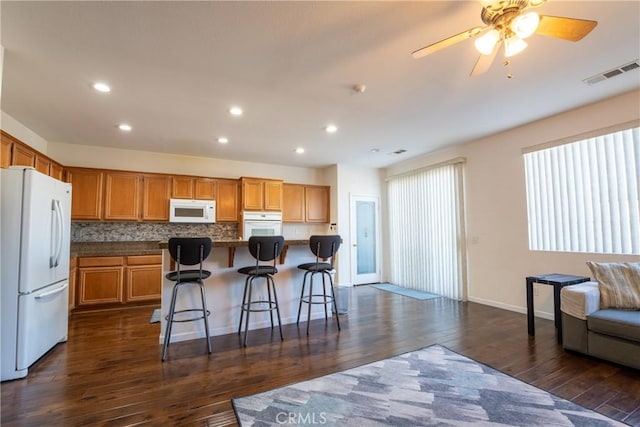 kitchen with a kitchen island, a breakfast bar, decorative backsplash, white appliances, and dark hardwood / wood-style flooring