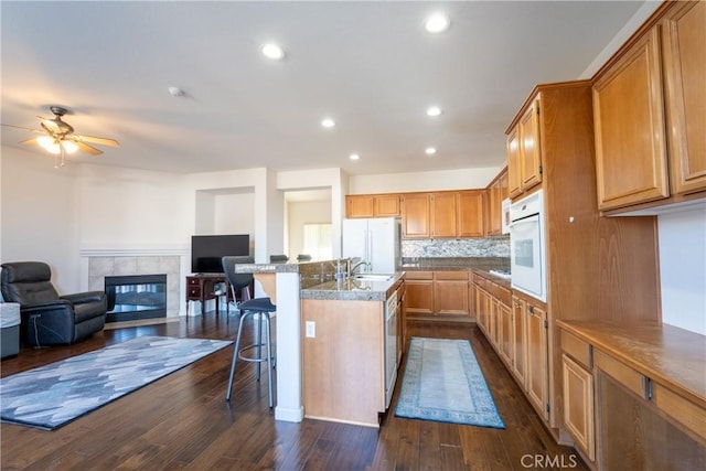 kitchen with a tile fireplace, sink, white appliances, a kitchen island with sink, and a breakfast bar area