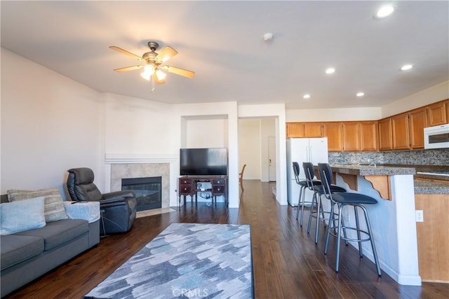 living room featuring ceiling fan, a tiled fireplace, and dark wood-type flooring