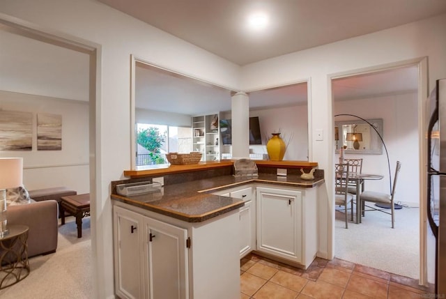 kitchen featuring ornate columns, dark stone countertops, white cabinets, light colored carpet, and kitchen peninsula