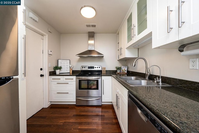 kitchen with wall chimney exhaust hood, white cabinets, appliances with stainless steel finishes, dark stone countertops, and sink