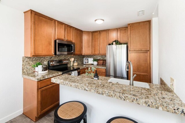 kitchen with a kitchen bar, stainless steel appliances, sink, backsplash, and kitchen peninsula