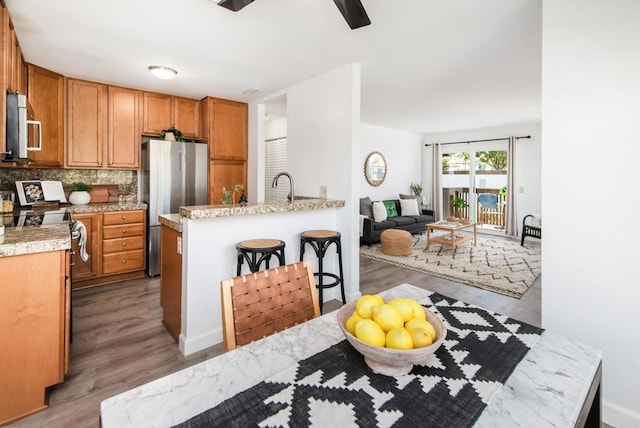 kitchen featuring a kitchen breakfast bar, appliances with stainless steel finishes, decorative backsplash, and light hardwood / wood-style flooring