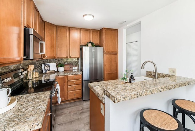 kitchen featuring kitchen peninsula, stainless steel appliances, a kitchen breakfast bar, light stone counters, and sink