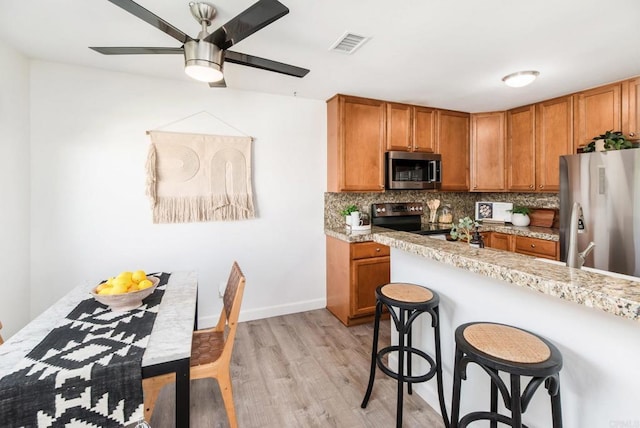 kitchen with ceiling fan, backsplash, light hardwood / wood-style flooring, appliances with stainless steel finishes, and a breakfast bar area