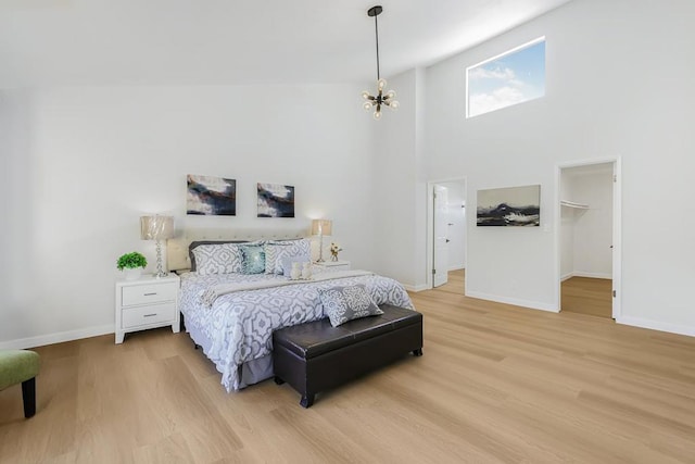 bedroom featuring a towering ceiling, a walk in closet, a chandelier, and hardwood / wood-style floors