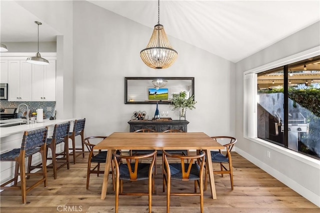 dining room featuring vaulted ceiling, a notable chandelier, light wood-style flooring, and baseboards