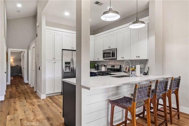 kitchen featuring tasteful backsplash, visible vents, appliances with stainless steel finishes, a sink, and a kitchen breakfast bar