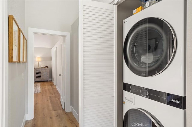 clothes washing area featuring stacked washing maching and dryer, light wood-style flooring, laundry area, and baseboards