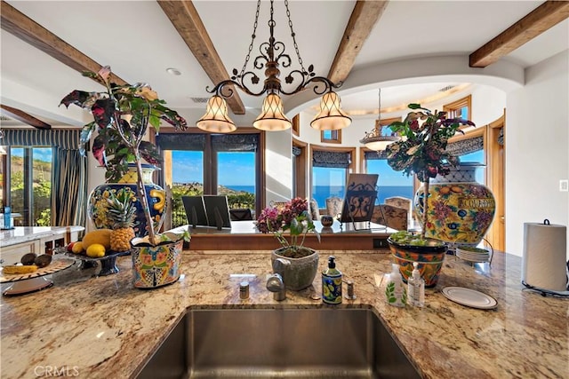 kitchen with decorative light fixtures, an inviting chandelier, beamed ceiling, and light stone countertops