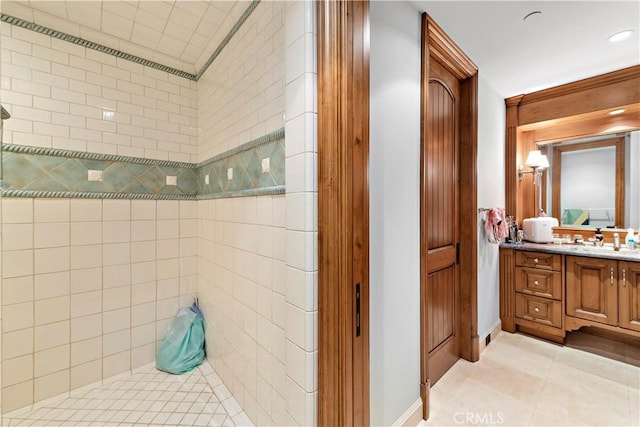 bathroom with tile patterned flooring, a tile shower, and vanity