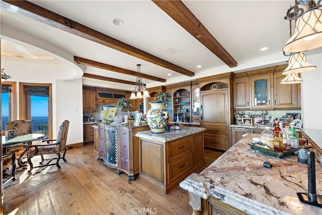 kitchen with light hardwood / wood-style floors, beamed ceiling, light stone countertops, pendant lighting, and a kitchen island