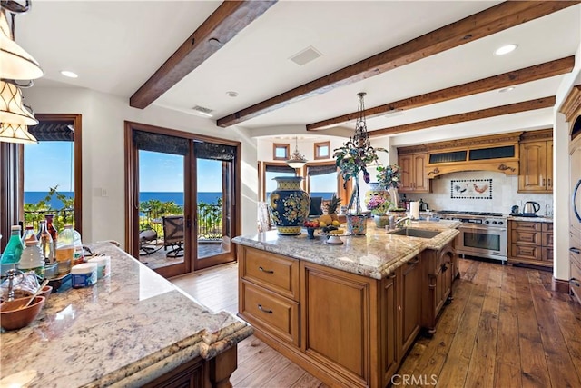 kitchen featuring beam ceiling, hanging light fixtures, double oven range, and a center island with sink