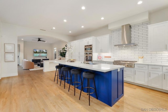 kitchen featuring a center island with sink, white cabinets, wall chimney range hood, and stainless steel gas cooktop